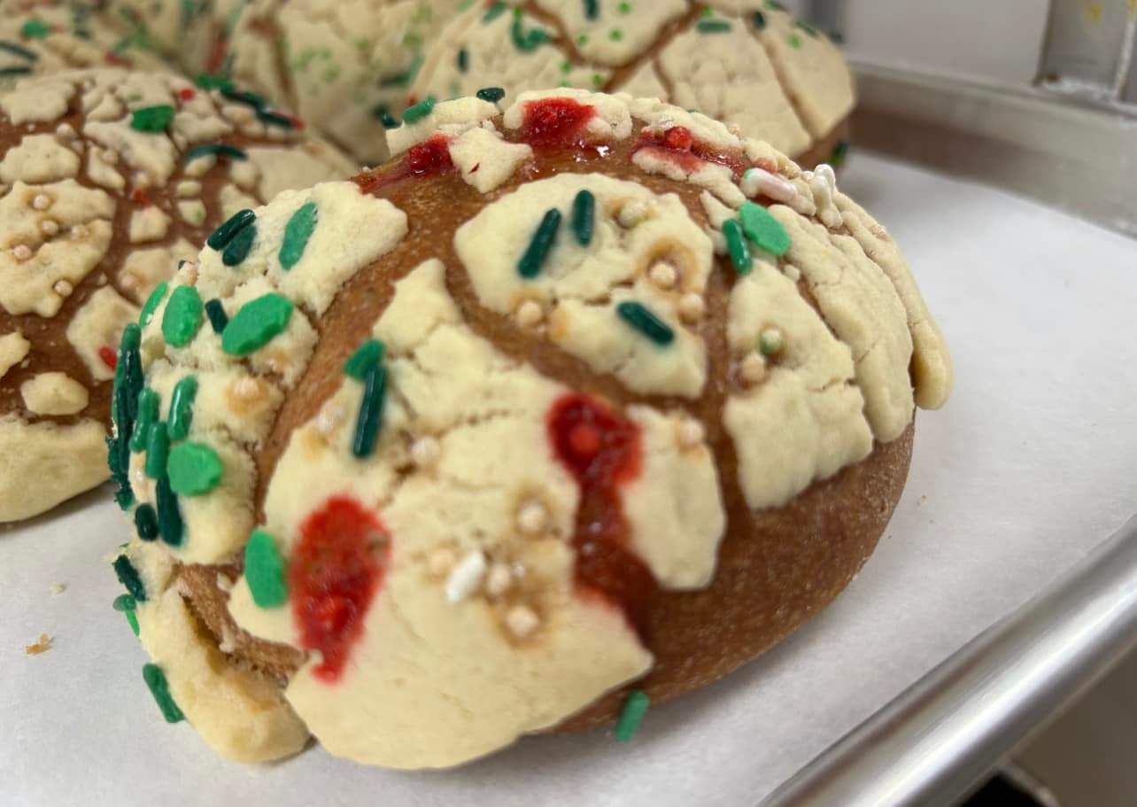 A festive, shell-patterned sweet bread decorated with colorful sprinkles and red accents rests on a white tray.