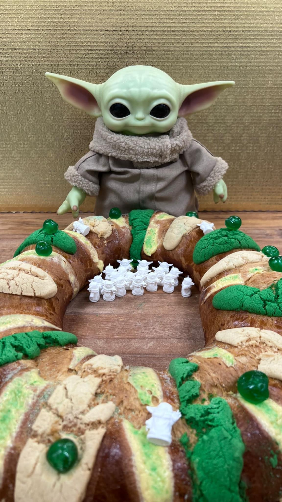 A Grogu (Baby Yoda) doll oversees a festive Rosca de Reyes cake adorned with numerous miniature Grogu figurines.