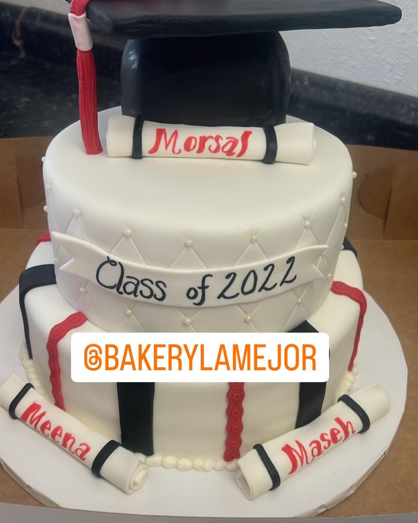 A white, multi-tiered graduation cake is topped with a cap and decorated with "Class of 2022" and student names.