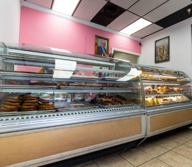 Glass display cases filled with an assortment of baked goods and pastries line a brightly lit bakery.