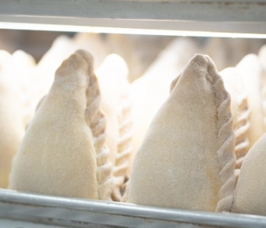 Multiple unbaked empanadas with crimped edges stand upright on a metal tray.